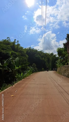 First-person video of a motorcycle ride on a sunny day on a countryside road that rises upwards and is surrounded by trees and plantations. Footage riding on the hinterland of Bandung, Indonesia