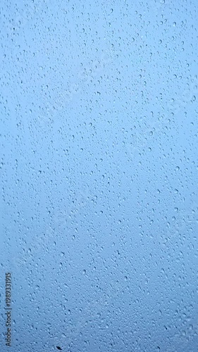 Water droplets gather on a window as rain falls outside on a cloudy morning.