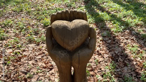 Wooden sculpture of hands holding heart, love and care concept, support and compassion, nature setting, symbolic art, outdoor scene with copy space