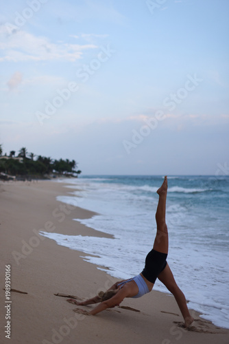 Sunrise yoga practiced on sandy coast. Flexible female athlete performing dynamic stretch at shoreline
