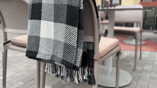 Plaid scarf draped over chair in cafe setting, cozy lifestyle concept, autumn fashion, comfort, casual interior scene, minimal aesthetic composition