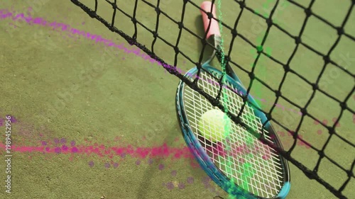 Tennis racket with ball tilting by net on green court as particles sweeping in, showcasing racket