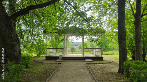 Wooden gazebo in a lush green summer park with a gravel footpath