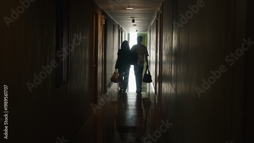 Bild auf Leinwand Tourists walking down dark hotel corridor with bags