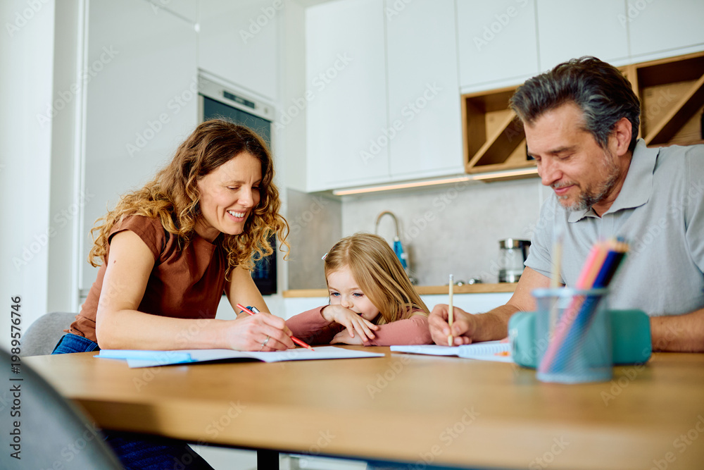Fototapeta premium Parents cheerfully helping their young daughter with school homework, supporting her education while learning together at home
