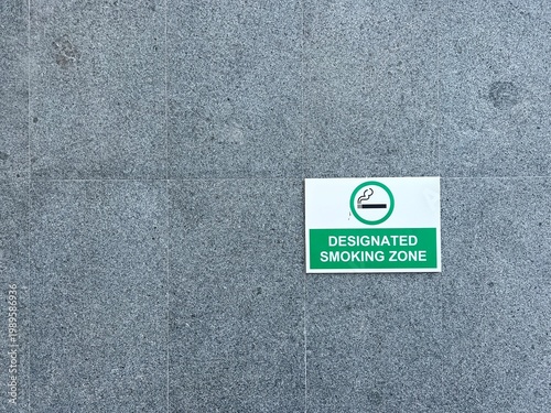 Obraz na plátne A green and white designated smoking zone information sign mounted on a grey granite stone wall in a public area