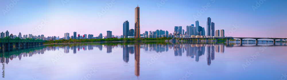 Fototapeta premium Seoul South Korea metropolitan city skyline panorama at sunset along the Han River, tranquil riverwalk open space landscape with skyscrapers and serene water reflections.
