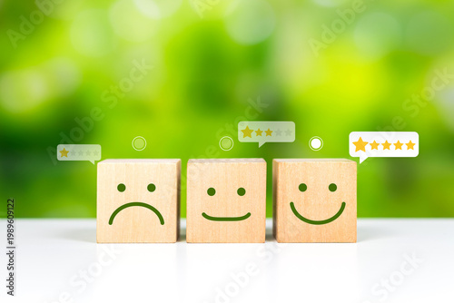 Wooden blocks with sad, neutral and happy faces and star ratings on natural green background. Satisfaction, service rating and positive feedback concept