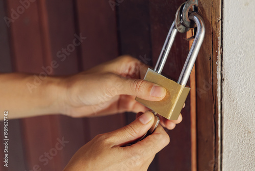 Securing the Entry: Hands Using a Key to Open a Brass Padlock on a Wooden Door