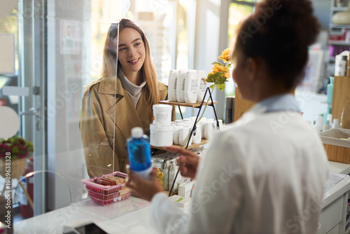 Schilderij op canvas Happy young woman talking to a pharmacist while buying a medicine in a drug store