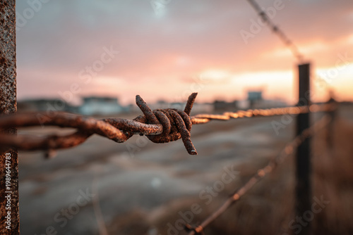 Rusty barbed wire at sunset creates a stark, moody atmosphere in a desolate landscape.