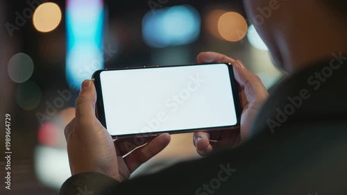 Person holding smartphone with blank screen in evening city lights