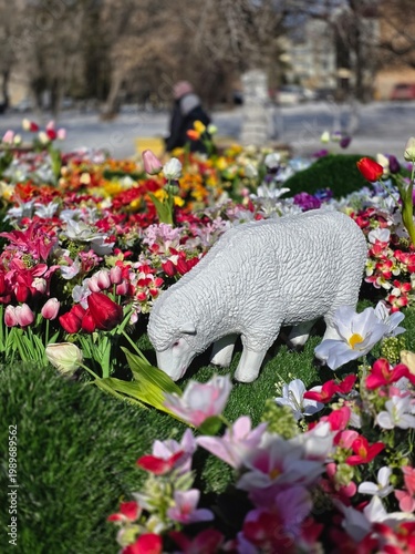 Decorative sheep statue on a vibrant flower bed in a public park.