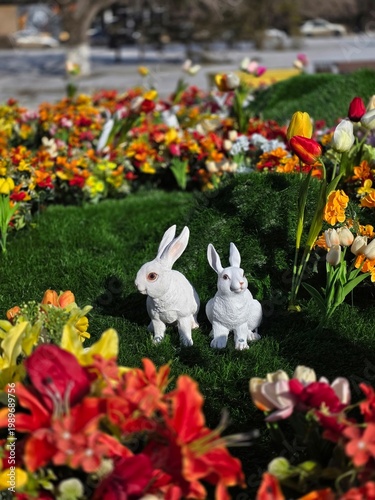 Decorative white rabbit statues on a vibrant spring flower bed.