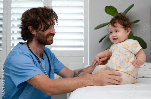 Photos Side view of a friendly male pediatrician in blue scrubs checking infant’s movem