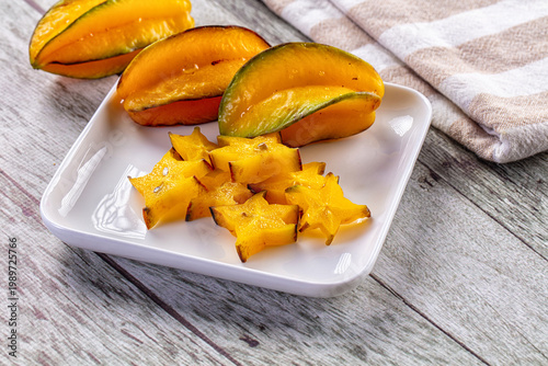 Foto Fresh sliced star fruit and whole carambola on a plate over a rustic wooden background