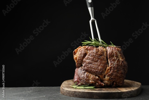 Foto Tasty beef steak with rosemary and carving fork on table against black background, closeup