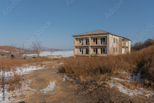 Bilde på lerret Abandoned two-story building with broken windows surrounded by dry grass and sno