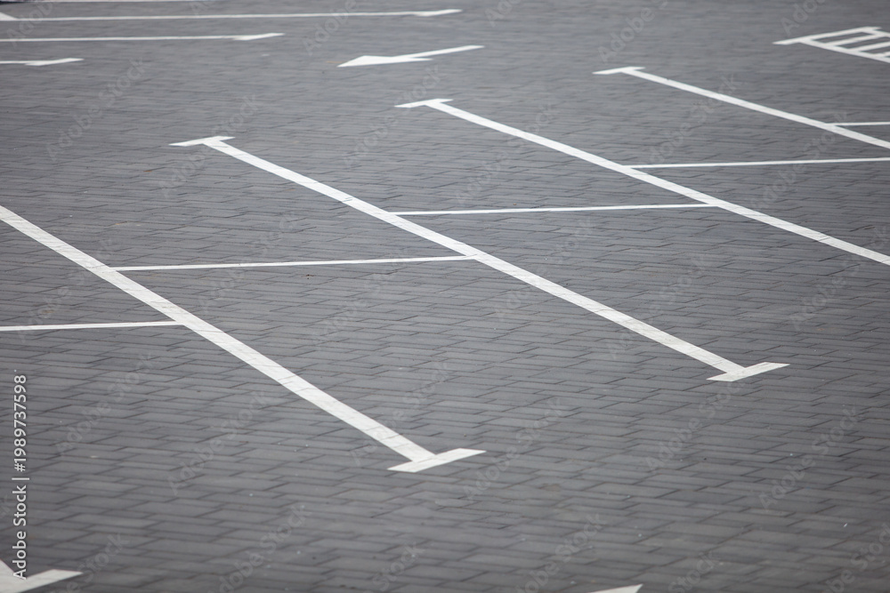 Fototapeta premium High-angle view of white painted parking lines and directional arrows on a gray paving stone surface at an empty outdoor parking area