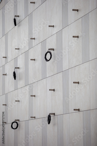 Quadro su tela Close-up of a modern ventilated facade with light beige stone tiles, featuring installed metal brackets and coils of black electrical wiring for future lighting or equipment