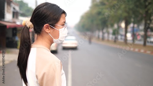 Back view of a young girl wearing a protective face mask looking at a foggy and polluted city road, PM 2.5 air pollution and environmental crisis concept