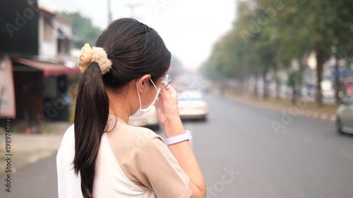 Back view of a young girl wearing a protective face mask looking at a foggy and polluted city road, PM 2.5 air pollution and environmental crisis concept