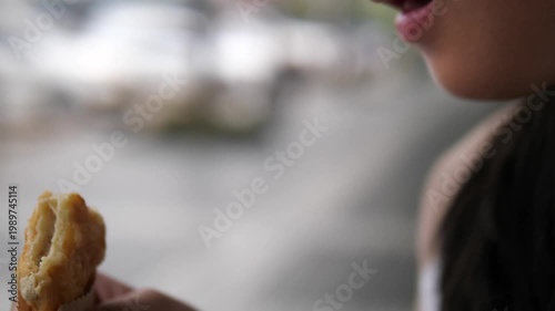 Close-up of young girl with glasses biting a delicious crispy sandwich or pastry, fast food and hungry lifestyle concept