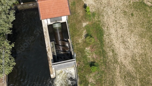 Archimedes Screw Water Pump: An Archimedes screw water pump mechanism is housed within a structure by a body of water, demonstrating an ingenious method of water displacement and flow control.