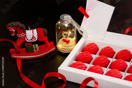 A white cardboard box with red shortcrust pastry nuts, with filling, on a black background, decorated with red ribbons and toys - a horse and a teddy bear in a jar