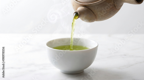 A serene scene of green tea being poured into a white ceramic cup on a marble countertop