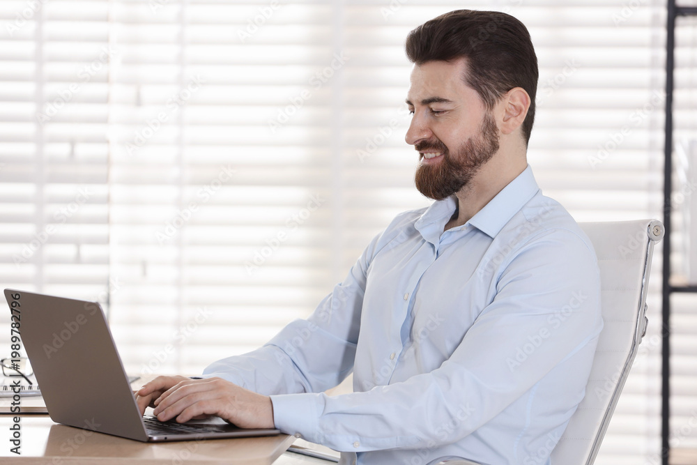 Fototapeta premium Handsome businessman working on laptop at wooden desk in office