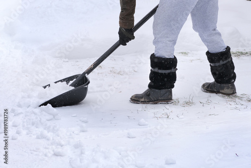 A man in warm clothes and gloves with a large shovel removes snow