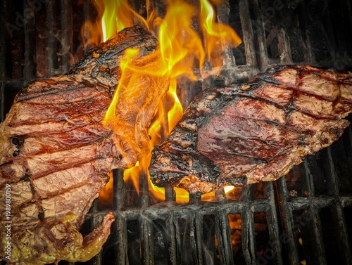 Two sirloin steaks grilling on barbecue with flames and smoke, close up of beef steaks cooking over open fire, juicy meat searing on grill, outdoor BBQ food preparation