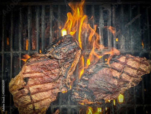 Two sirloin steaks grilling on barbecue with flames and smoke, close up of beef steaks cooking over open fire, juicy meat searing on grill, outdoor BBQ food preparation