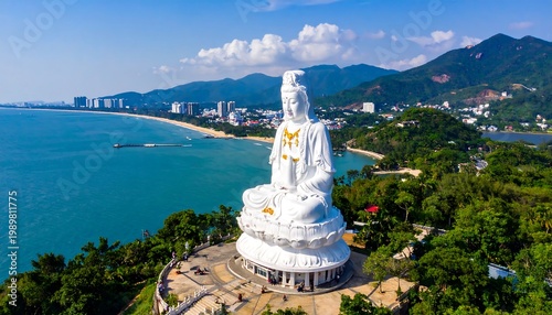 Aerial view of a large white seated statue overlooking a coastal city and ocean. Mountains are visible in the distance