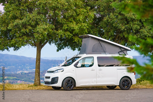 Camping setup with rooftop tent on van vehicle in green area during daytime in a natural setting