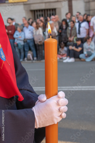 Hands with penitent gloves holding a candle in a procession