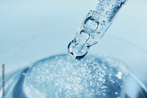 Glass dropper applying liquid with bubbles to petri dish in medical lab setting