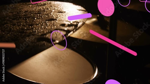 Two metallic cymbals on stands catching warm backlight, water droplets shifting, graphics drifting