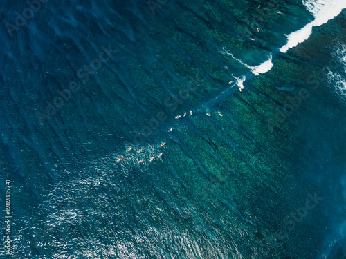 Drone shot of surfers riding waves over coral reef in Bali, tropical surf trip