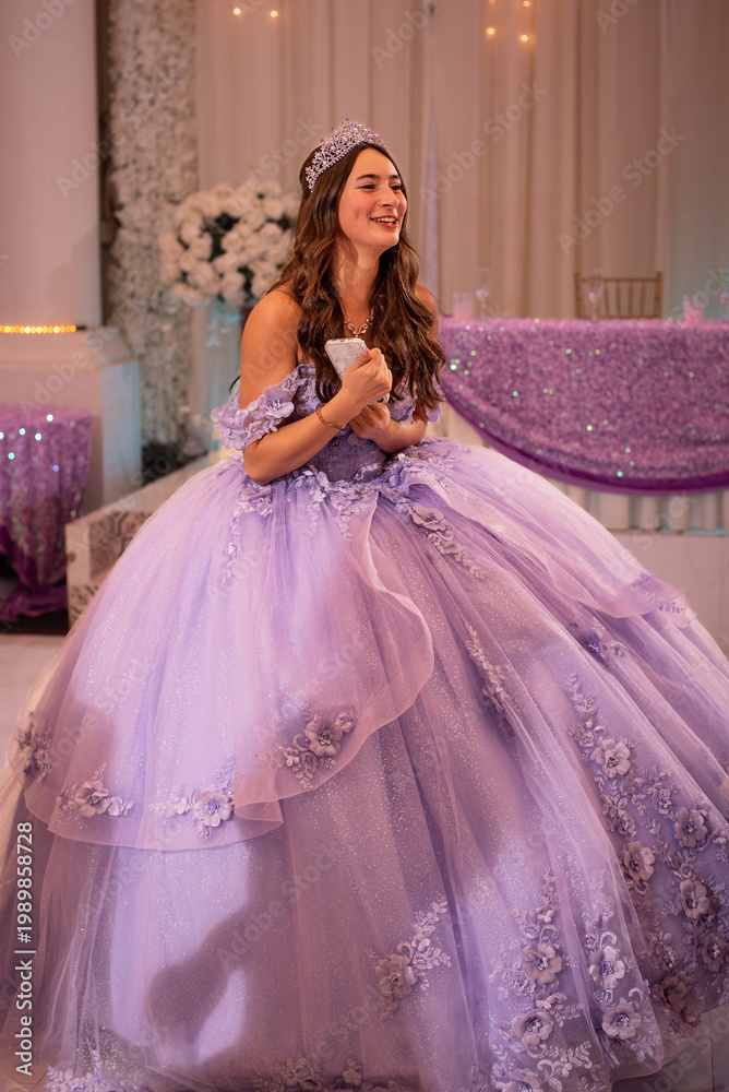 Fototapeta premium Quinceañera clutches her phone and smiles on the dance floor in a stunning purple dress
