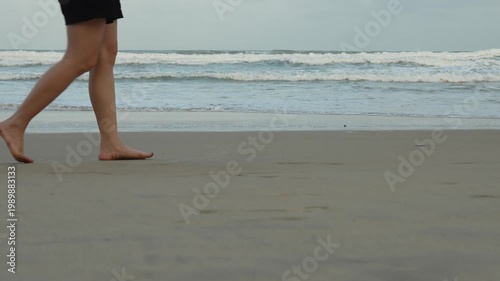 Close-up at human heel barefoot during walking on fine sand beach with water wave splashing. People travel in nature footage scene.