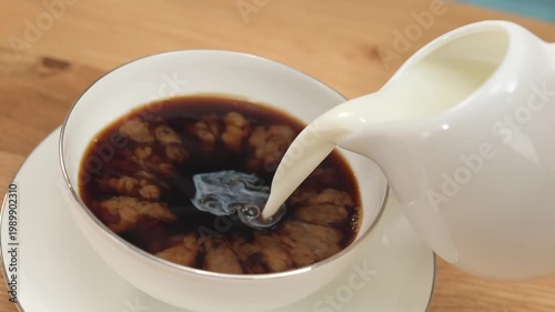 Cream pouring into hot coffee in glass cup creating smooth swirl, copy space
