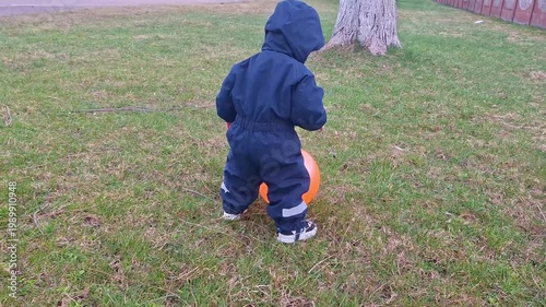Little toddler playing with orange balloon outdoors