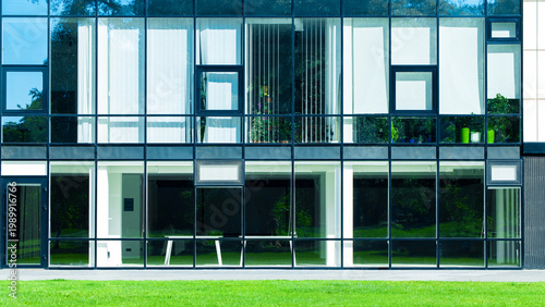 Modern glass facade building with green lawn in front on a sunny day