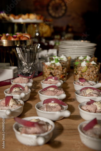 Elegant buffet with small gourmet dishes served in ceramic bowls, featuring meat, creamy sauce, and pickled garnish, set in a warm, upscale event ambiance.