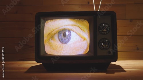 Closeup shot of eye looking around playing on a vintage television set with wooden background.