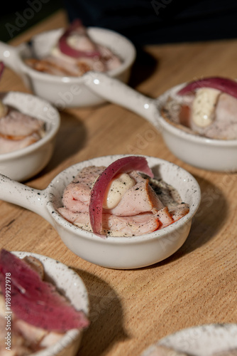 Close-up of gourmet appetizer in small ceramic dish with sliced meat, creamy sauce, and pickled garnish, styled for an elegant catering or fine dining event.