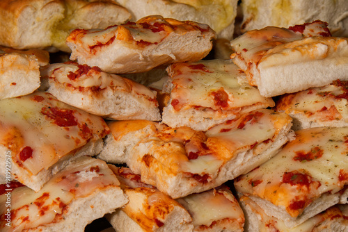 Stacked slices of cheesy pizza focaccia with tomato sauce, golden crust and melted cheese, warm and appetizing comfort food close-up.
