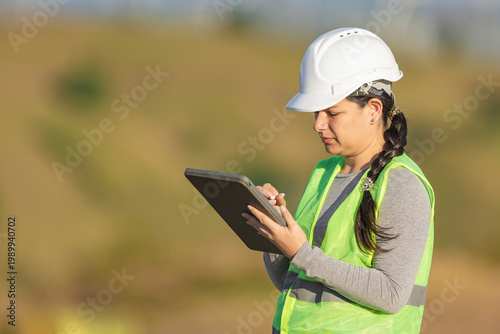 Female engineer wearing hard hat taking notes on tablet